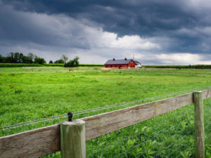 Storm clouds hovering over a farm with a fence in the foreground.