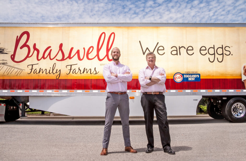 Two men stand in front of a braswell family farms truck.