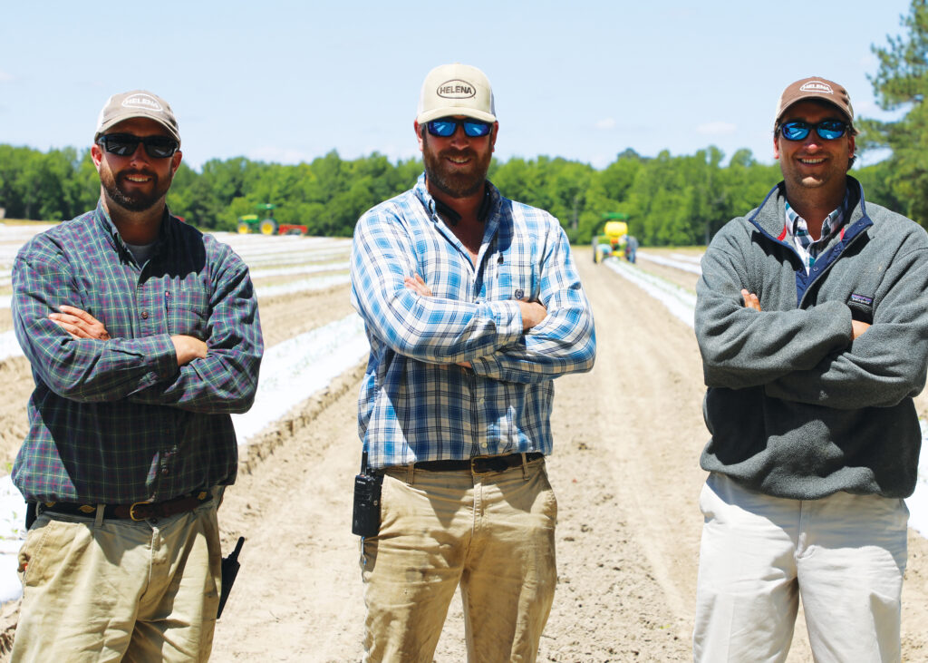 Three men stand in a plowed field. 